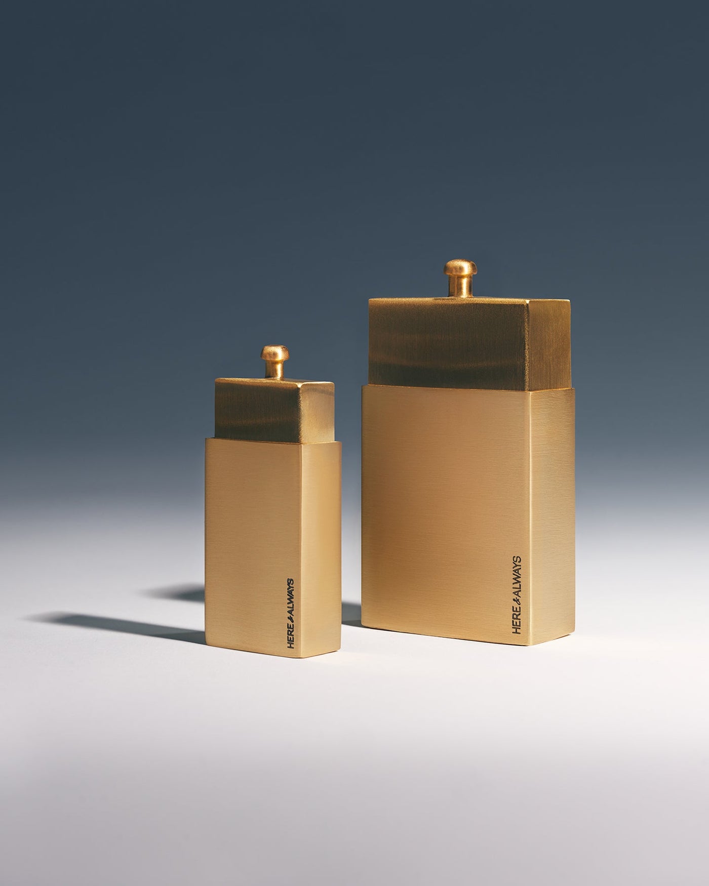 Rear view of Little and Big brushed brass matchbox showing Here & Always brand signature engraving, studio shot with blue gradient background | Here & Always